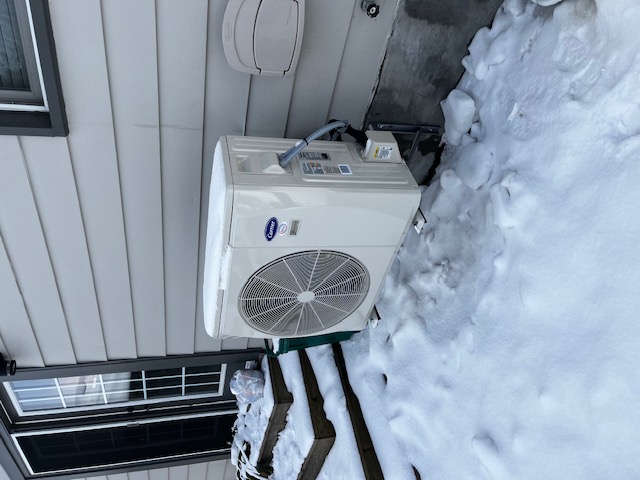 Carrier outdoor heat pump on a raised base beside a house in snowy conditions