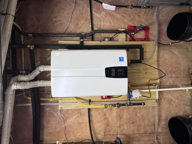 Wall-mounted Navien tankless water heater with connected piping and overhead vents